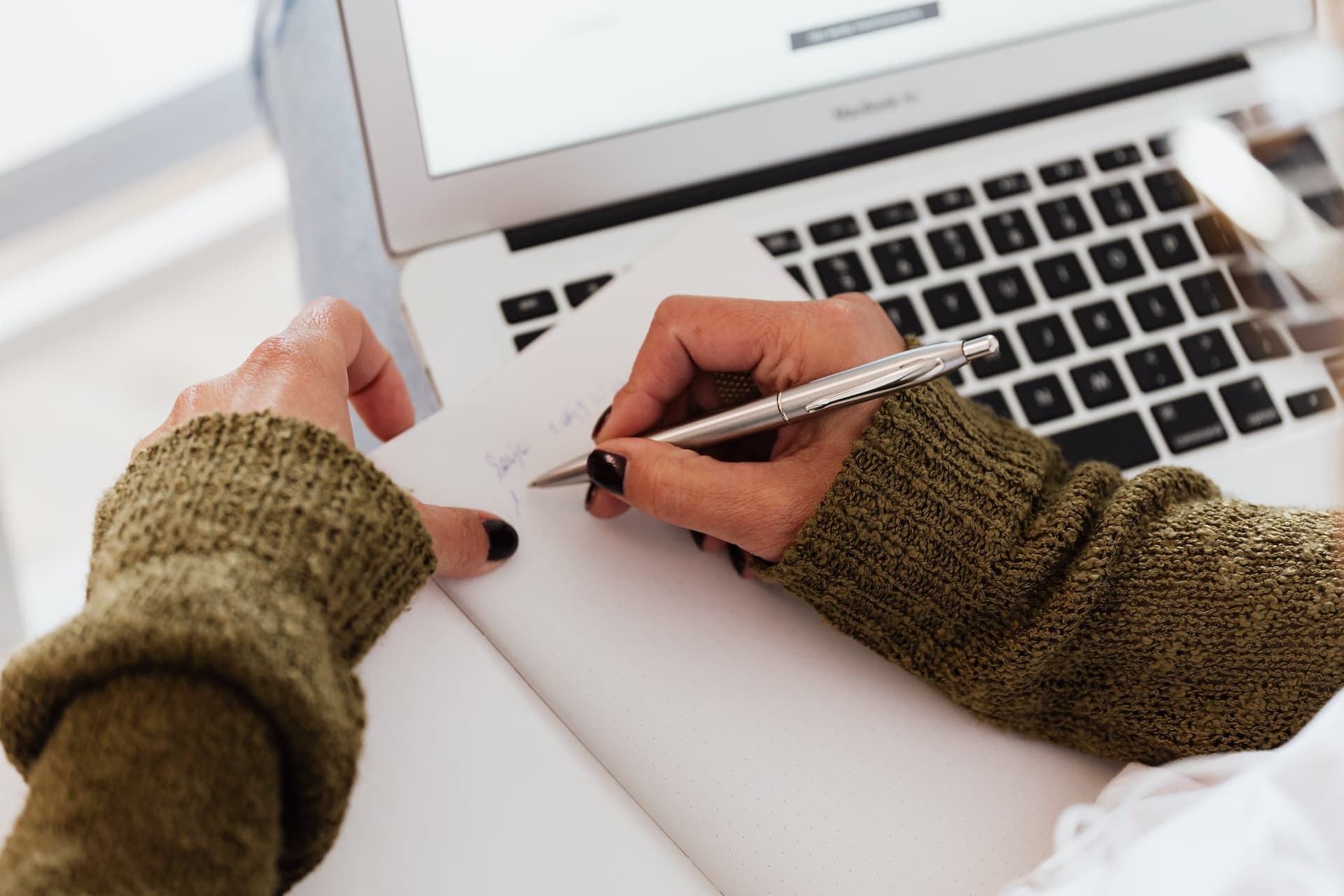 Person filling out a notebook over a computer